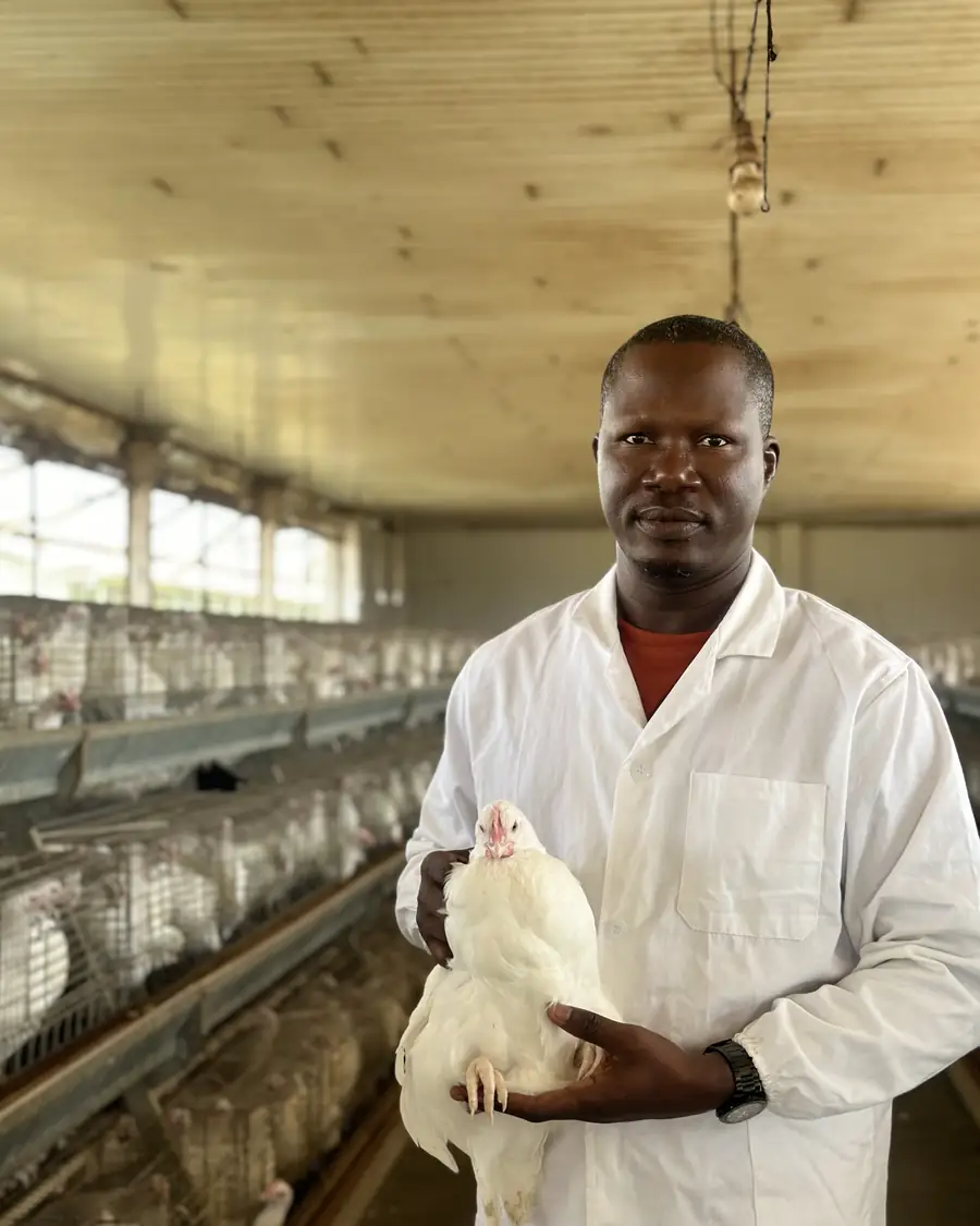 Le Dr Benoît Amoussou tient une poule blanche dans le bâtiment d'élevage
